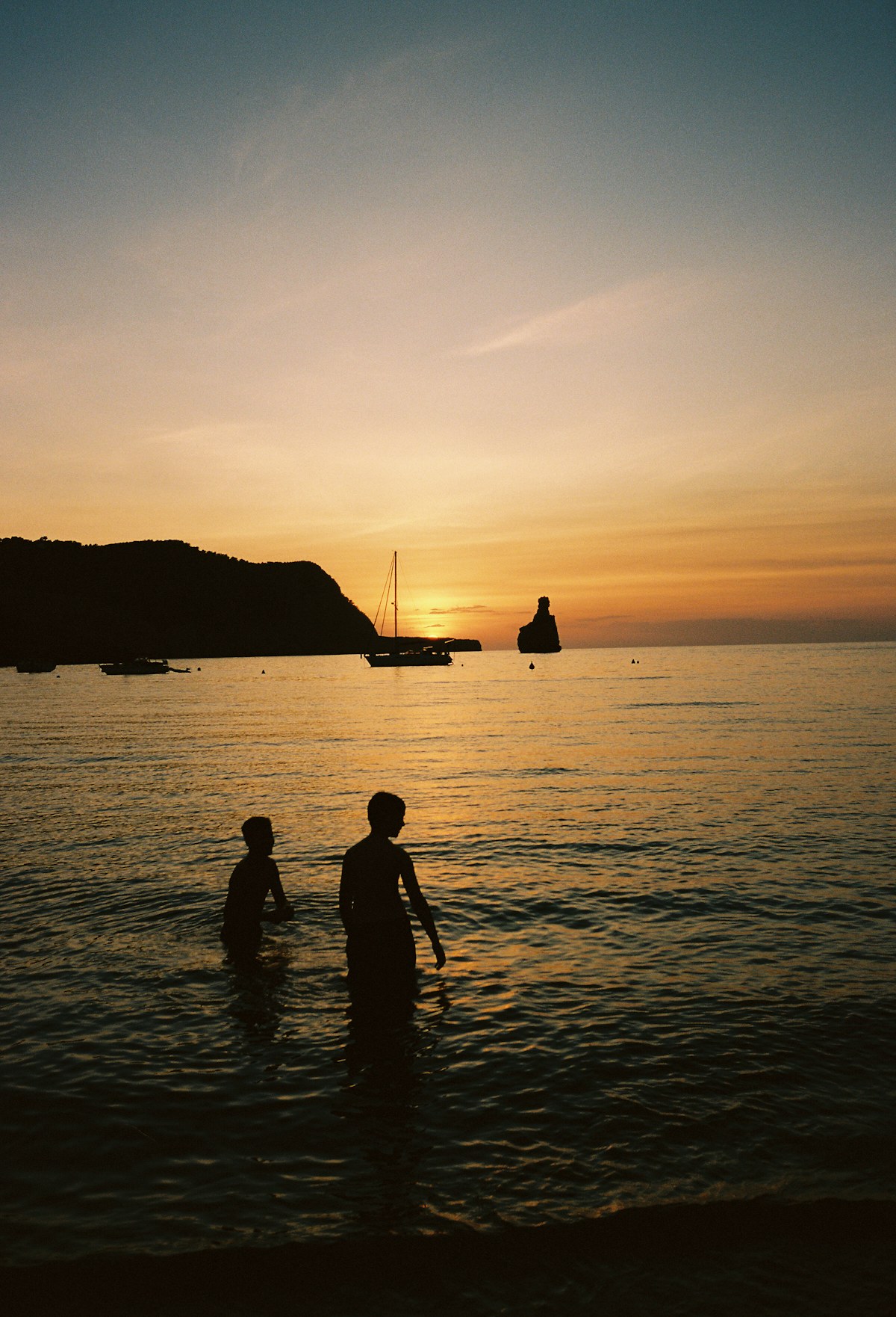 Two silhouettes standing in the sea as the sun sets over Ibiza